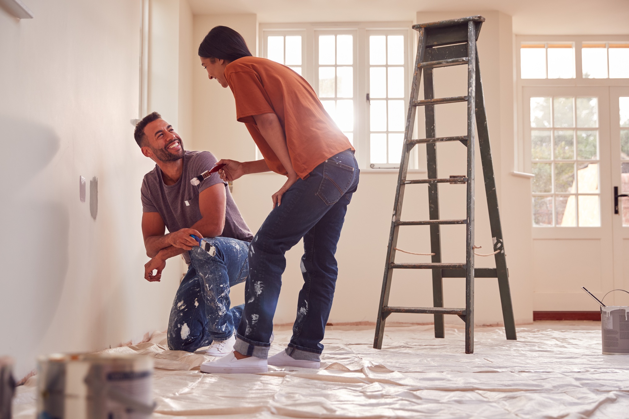 Couple Painting Test Squares On Wall As They Decorate Room In New Home Together